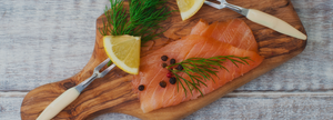 smoked salmon on a wooden cutting board with slice of lemon capers dill